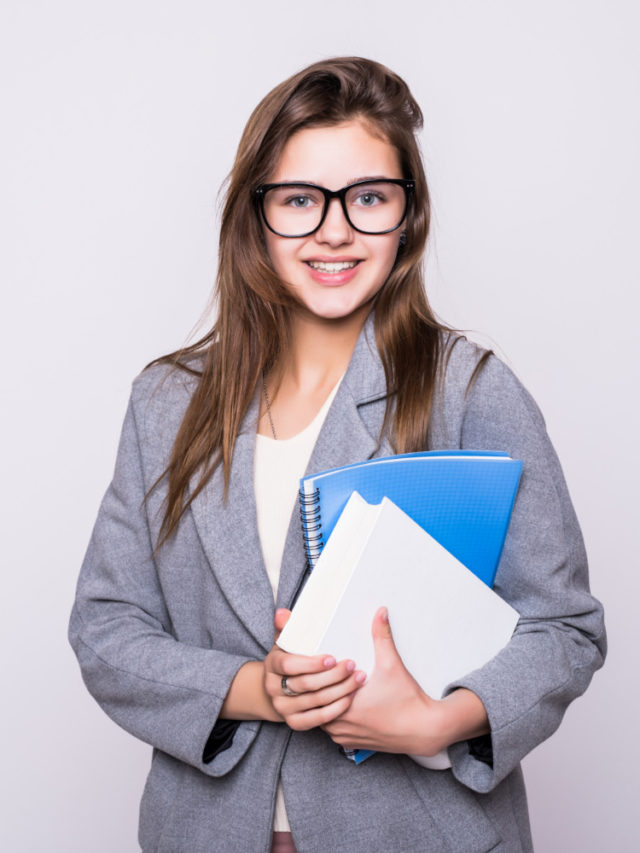 cropped pretty young student with big glasses near some books smiling white background